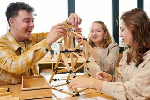 Drie studenten bezig met het bouwen van een toren met houten balkjes