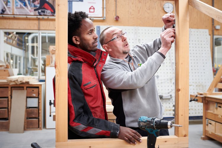 Docent laat student zien hoe hij een kozijn in elkaar zet in de werkplaats
