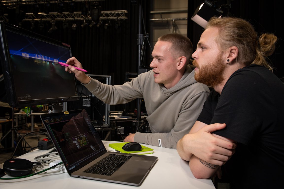 Een student 'broadcast technicus' wijst aan een andere student iets aan op een beeldscherm