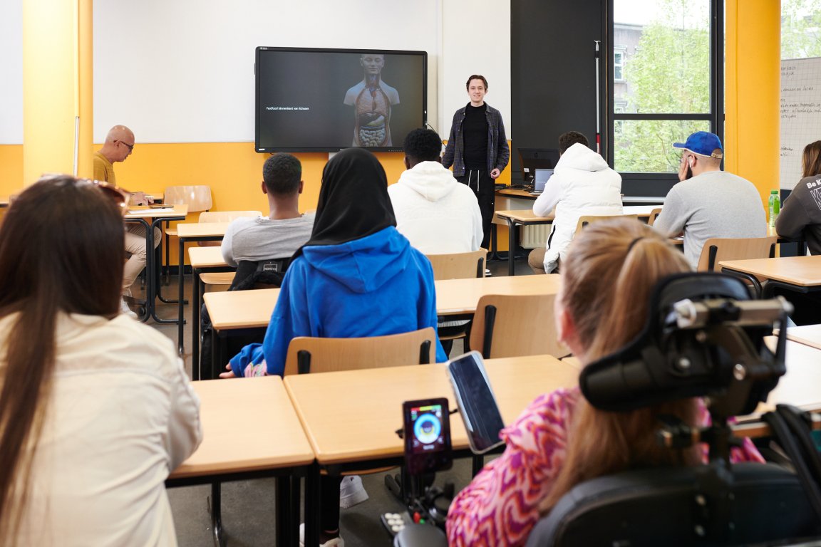 Klas met leerlingen die allemaal kijken naar de docent voor de klas en de presentatie op het scherm