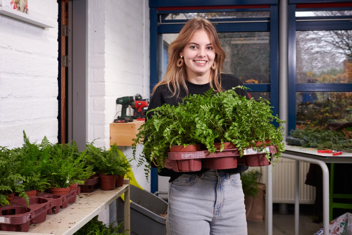 Student 'vakbekwaam medewerker groene stylist' in een klaslokaal met een selectie groene plantjes in haar handen