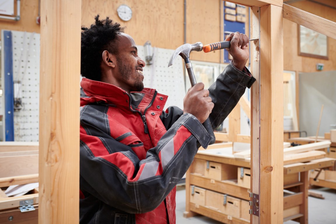 student met hamer in zijn hand bezig met het maken van een kozijn