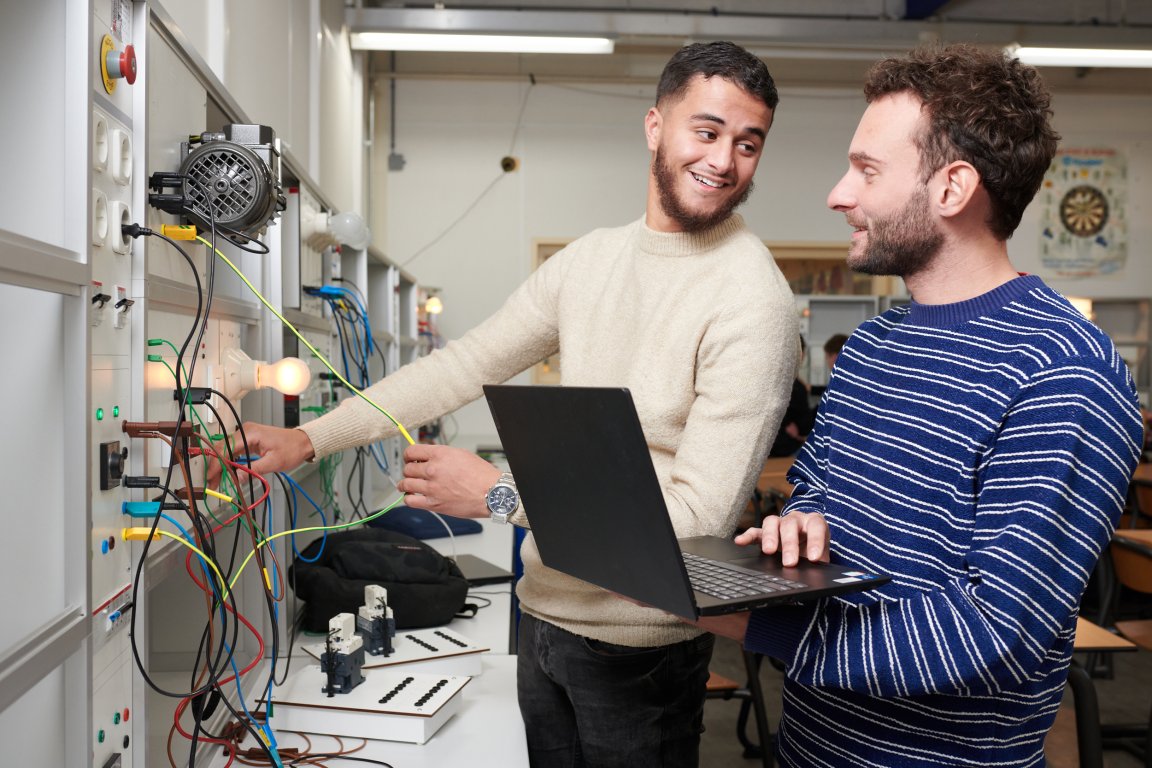 Docent controleert het werk van een student elektrotechniek