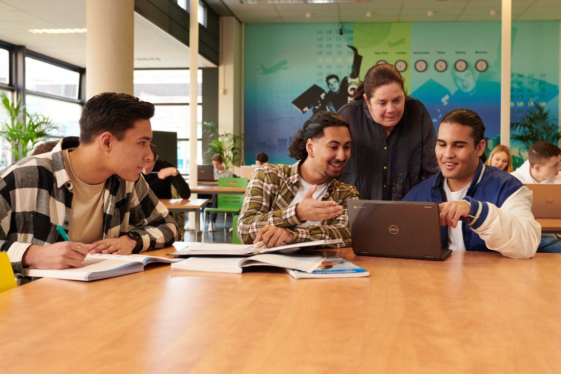 Docent kijkt met twee studenten in de klas mee op hun laptop 