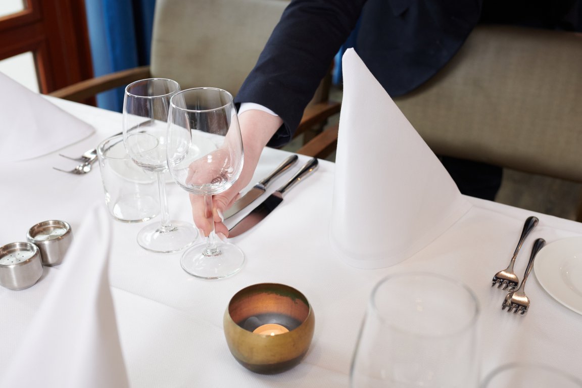 Deel van een gedekte tafel in een restaurant waar nog een extra wijnglas wordt neergezet