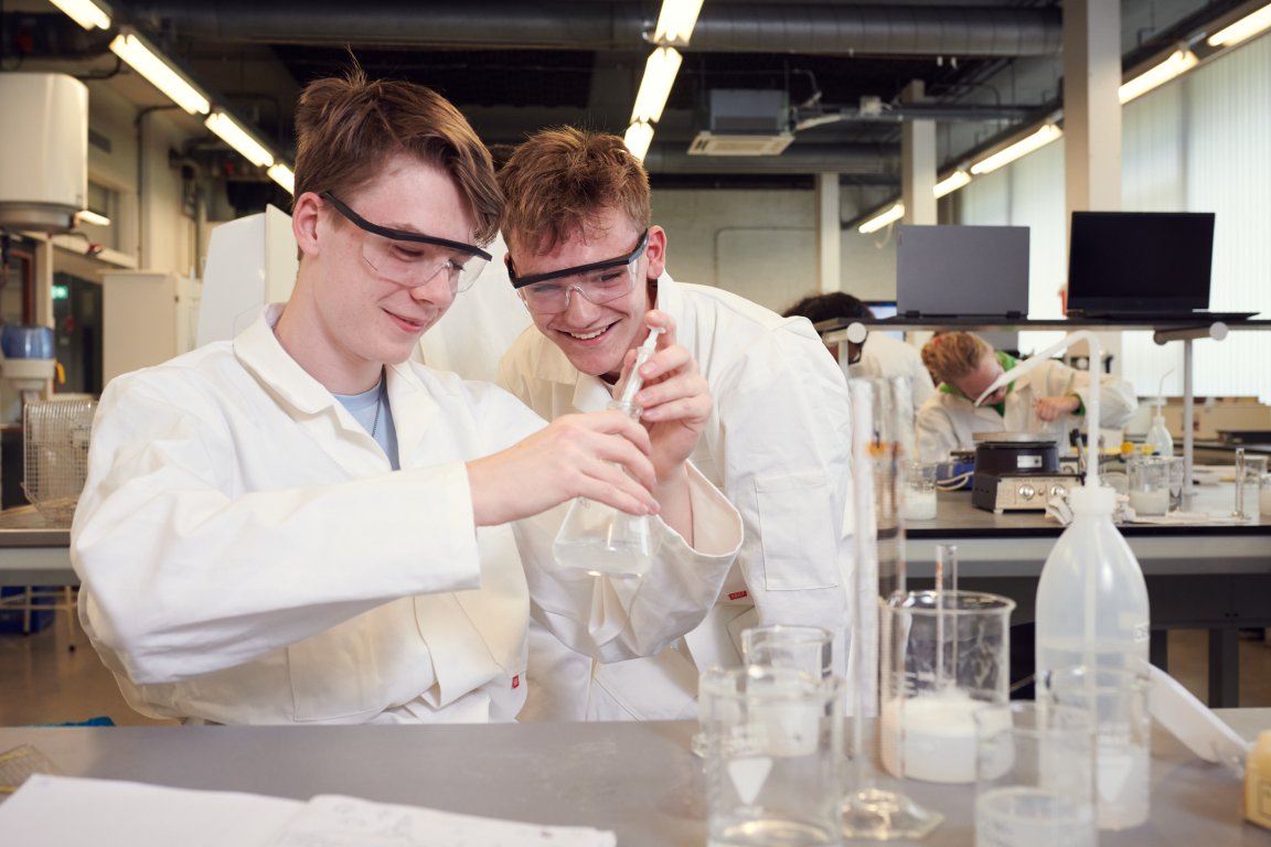 Twee studenten bezig met een substantie in een kegelvormig glas in schoollab