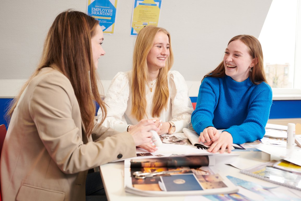 Drie lachende studenten marketing en communicatie met tijdschriften voor zich op tafel