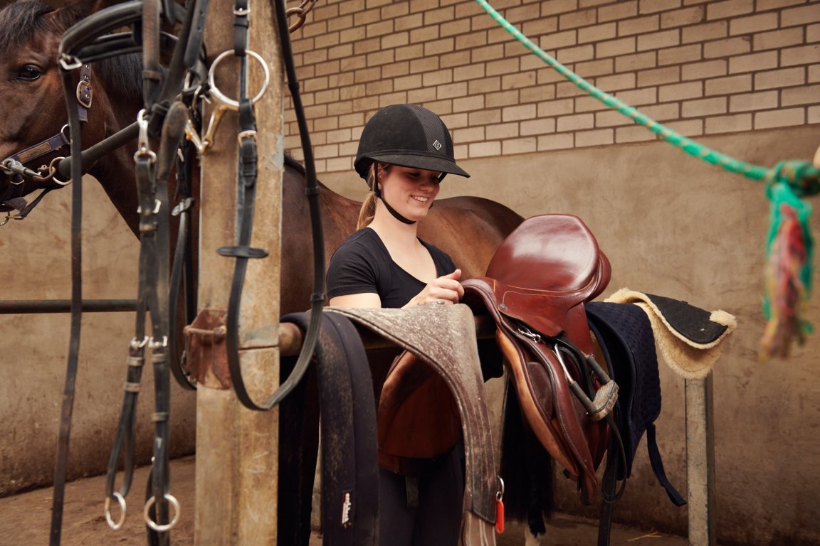 Student bezig met het opzadelen van een paard