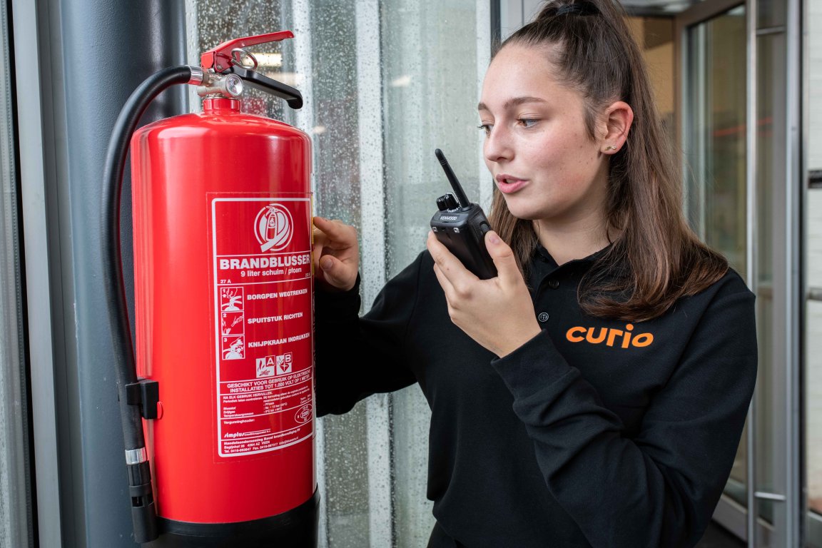Student beveiliging leest informatie op die op brandblusser staat en geeft dit door via de portofoon